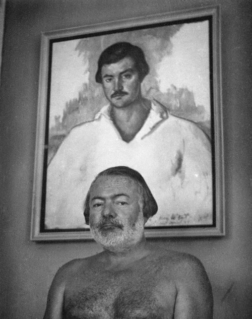 Hemingway at the Finca Vigia, in 1952, posing in front of Waldo Peirce’s 1929 oil portrait, &l
