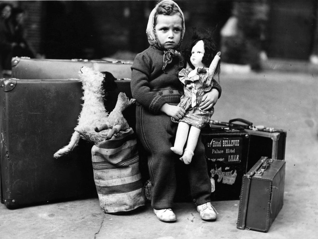 historicaltimes:  A nervous little girl waits with her dolls and her luggage before