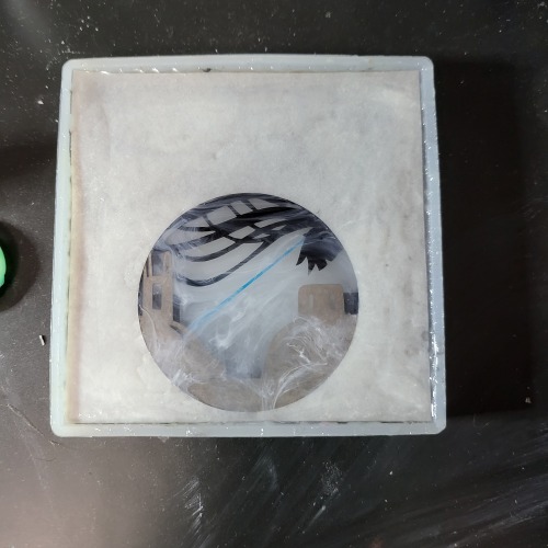 The paper layers can be glimpsed through a large circle cut out of a white square of paper at the top of the mold. More white swirls of ink have been added to the most recent layers.