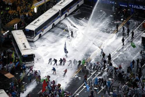 Protesters in South Korea attempt to move buses that are blocking their protest while being shot wit