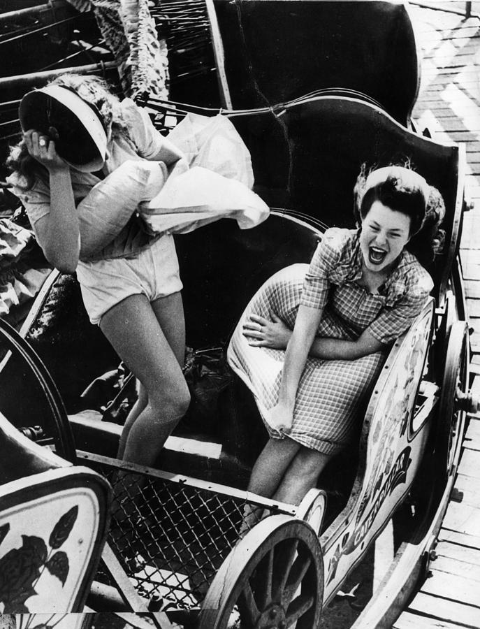 undr: Kurt Hutton. Two young women having trouble with their skirts on a fairground