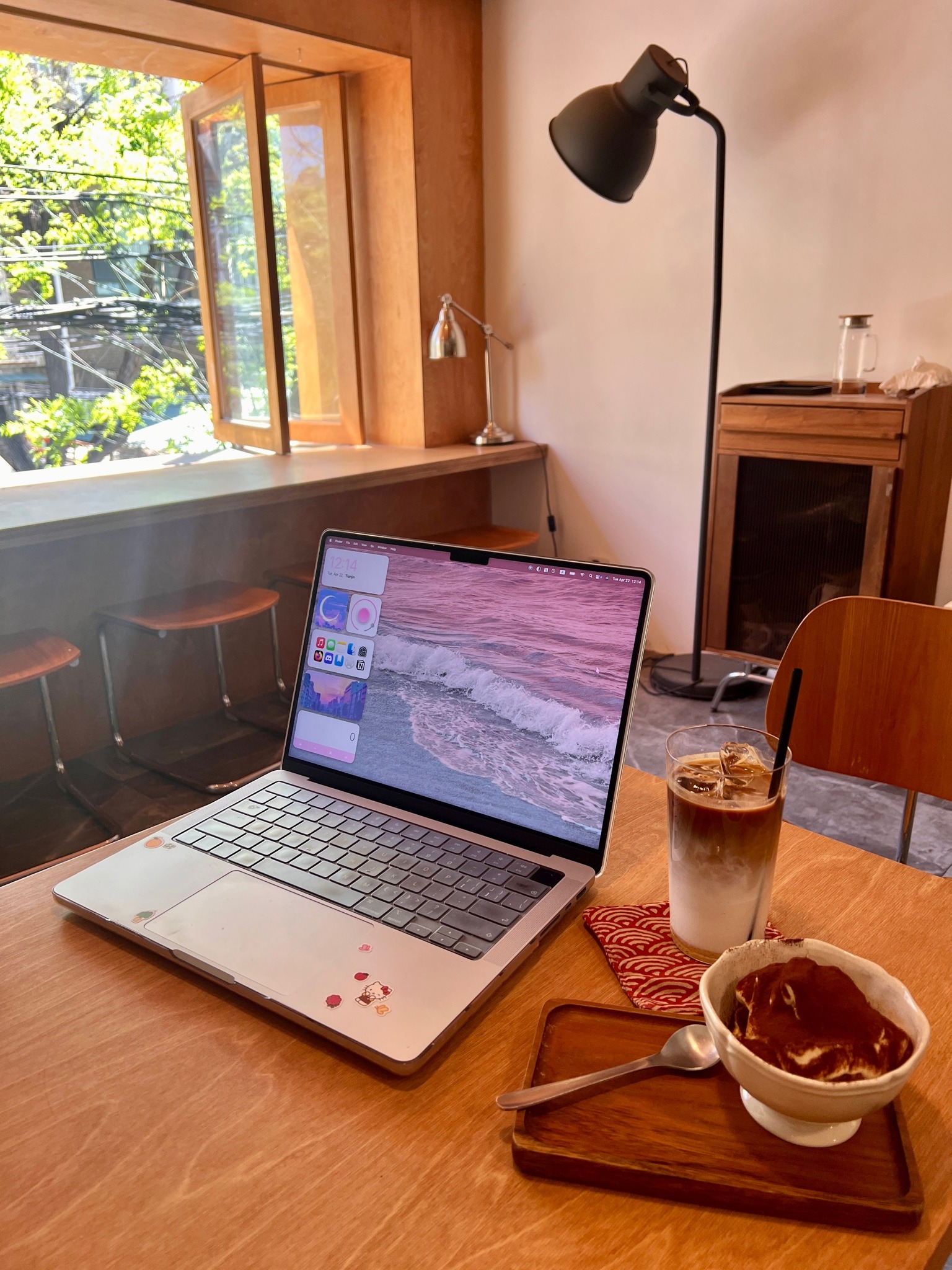 An iced latte and tiramisu on the table next to an open laptop