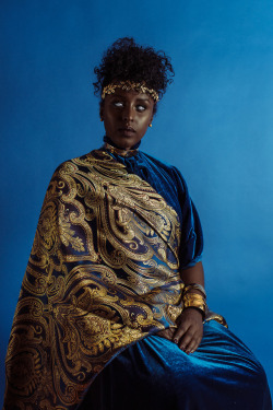 boydetective:  bobbyrogers: The Blacker the Berry: Chapter • IV Photography by Bobby Rogers  [Caption: Image of a model sitting and facing the camera against a blue background. The model has dark skin and greyish-white eyes. Their hair is kinky and