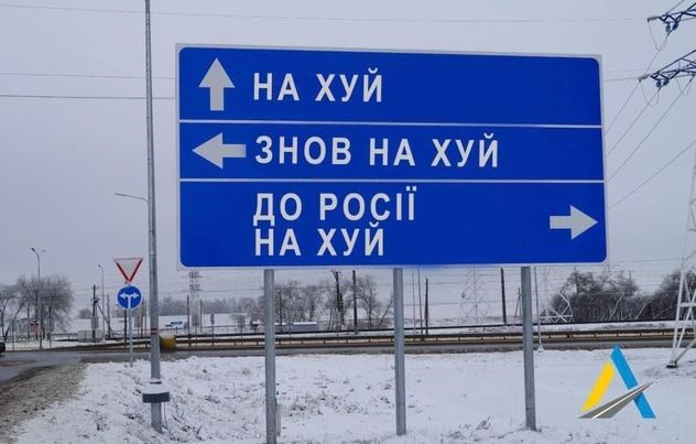 A big road sign at an intersection, the type that gives directions for straight on, left and right. The text is in Ukrainian.