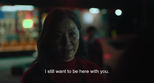 A screencap from the film Everything Everywhere All At Once. A middle-aged woman, Evelyn, is speaking to her daughter, Joy, with tears in her eyes. The caption reads: 'I still want to be here with you.'
