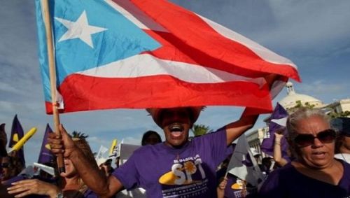 indigenous-caribbean:A member of a labor union shouts slogans while holding a Puerto Rico flag durin