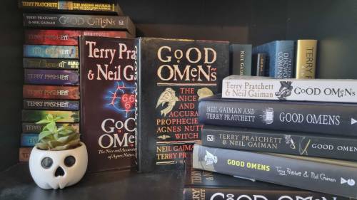 A bookshelf showing multiple copies of the book Good Omens by Neil Gaiman and Terry Pratchett.