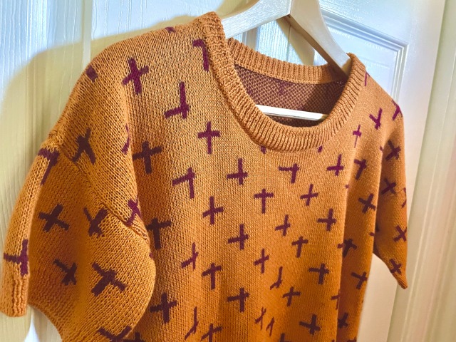 A closeup of a short sleeved yellow sweater hanging on a closet door.