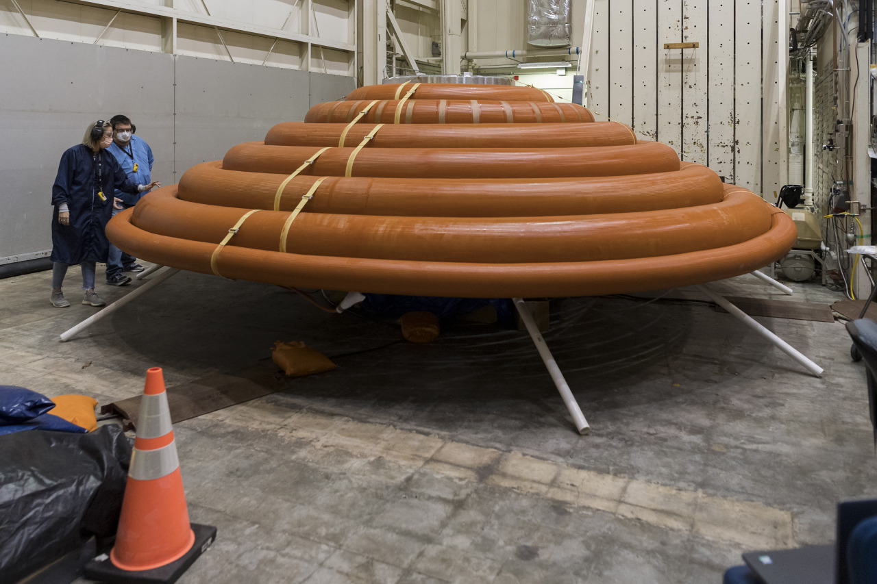 Engineers at NASA's Langley Research Center are standing next to an orange stack of inflated test rings atop a stand during the final test of the inflation system in Jan. 2022. The inflation system is one component of the LOFTID re-entry vehicle demonstration.