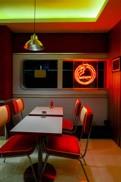 A Pin-Up Dining Area With A Glowing Sign For Permission To Smoke by Nikita Sursin.