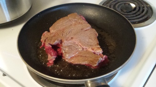A chuck roast being seared in a frying pan.