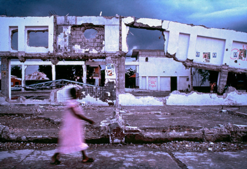 20aliens:HAITI. Gonaives. 1986. Passing in front of ‘Dechoukajed,’ a wrecked warehouse. By Alex Webb.