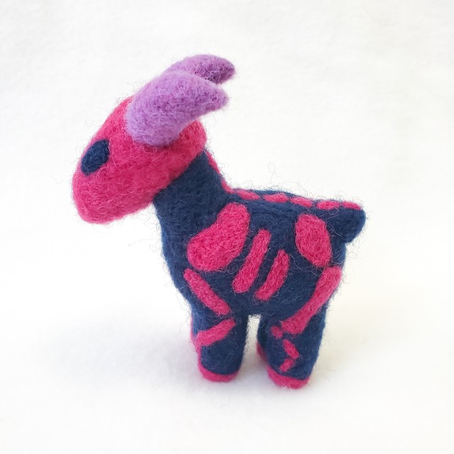 A photo of a dark blue needle felted ewe with purple horns and a pink skeleton pattern. The colors are in reference to the bisexual flag.