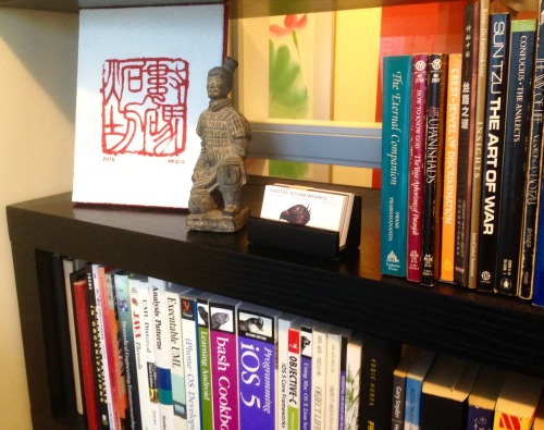 My office bookshelf featuring a recent canvas by co-conspirator Nezua &ndash; a rendering of our com