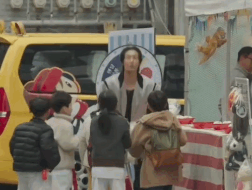 doyoung throwing bags of plushies in the air, surrounded by children that try to grab the bags