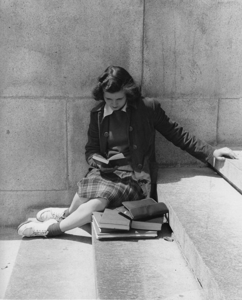 books0977:Student, dressed for class, reading on steps, 1950s.“I am reading six books at once,