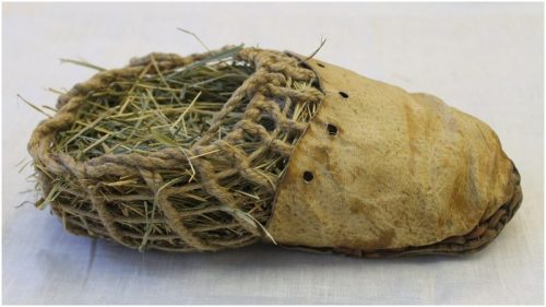 a reconstruction of the shoe worn by otzi the ice man. it is made of an outer layer of bear leather with the back half made of knotted twine, stuffed with dried grass