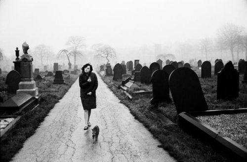 undr:John Bulmer. Woman and a cat walk through a cemetery in Wakefield West Yorkshire. 1964