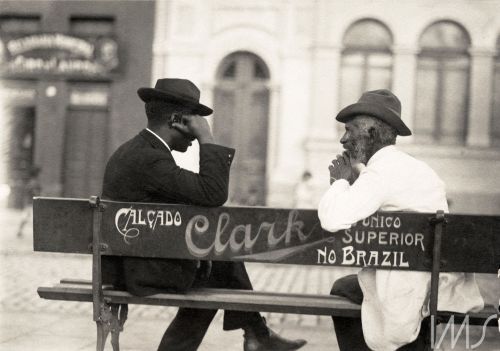 1) Retrato de homem idoso recostado em grade metálica da rua São João (circa 1910)2) Homens conversa