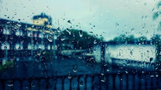 A rainy day seen through a window. The camera focused on the raindrops on the window, rendering the cityscape beyond blurry.