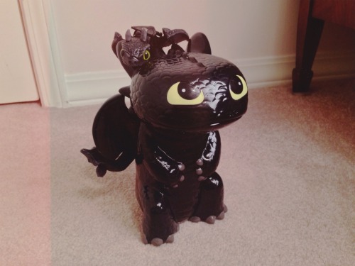 My brother got me a Toothless piggy bank Had to put my little toothless twin dragon doll on top of 