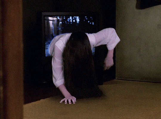 A GIF of a ghost with long black hair crawling out of a television screen.