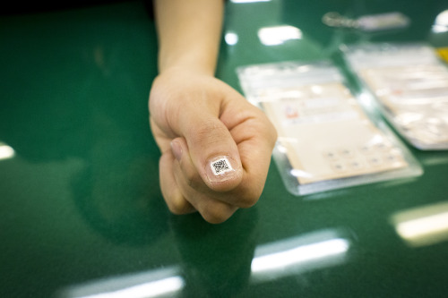 SAITAMA, JAPAN - DECEMBER 16 : A government employee demonstrate the QR nail sticker to a thumb to h