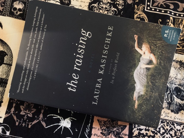 Pictured is THE RAISING (with cover art depicting a young woman lying in the grass) against vintage Gothic material showing skulls and other dark images. Photo by AHS.