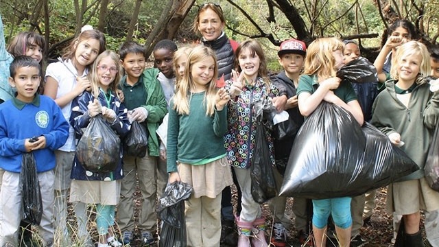 young children holding bags of trash after an outdoor cleanup accompanied by a teacher