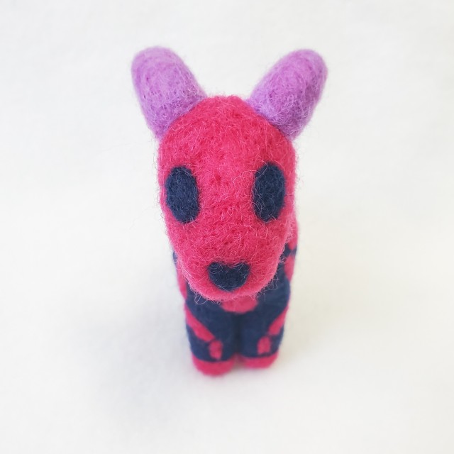 A photo of a dark blue needle felted ewe with purple horns and a pink skeleton pattern. The colors are in reference to the bisexual flag.