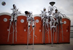 Stiltwalkers rest on a row of port-a-potties while rehearsing