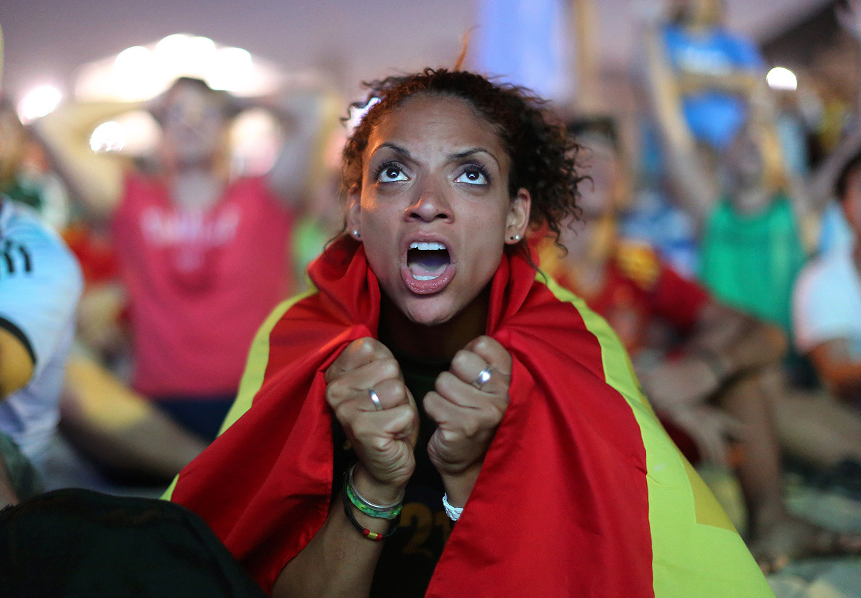From The 2014 World Cup, Part I, one of 36 photos. Wrapped in a Spanish national flag, a soccer fan reacts in frustration as she watches the live broadcast of the World Cup match between Spain and the Netherlands inside the FIFA Fan Fest area on...