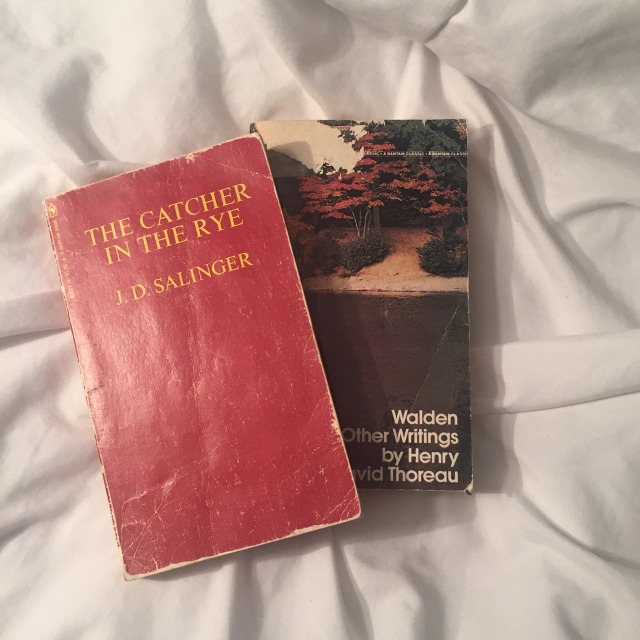 on white sheets sits two books: the bottom most book is Henry David Thoreau's 'Walden and Other Writings' and the top book is J.D. Salinger's 'The Catcher in the Rye'.