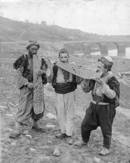 tanyushenka:Three men standing in a dirt field eating large pieces of flatbread Mesopotamia (undated