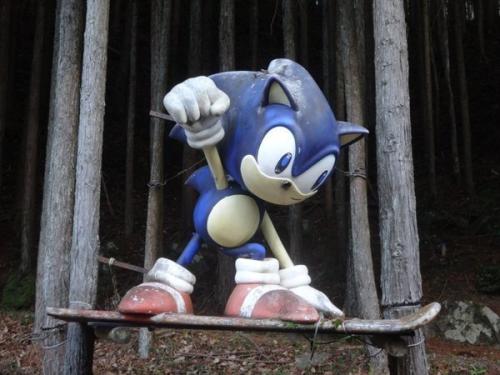 thivus: pr0jectneedlemouse: In the remote mountain forests of Nabari, Japan, there is a giant Sonic statue - purchased from a now-defunct SEGA World location, and nailed to some trees on the side of a rural highway. shrine to a local god 