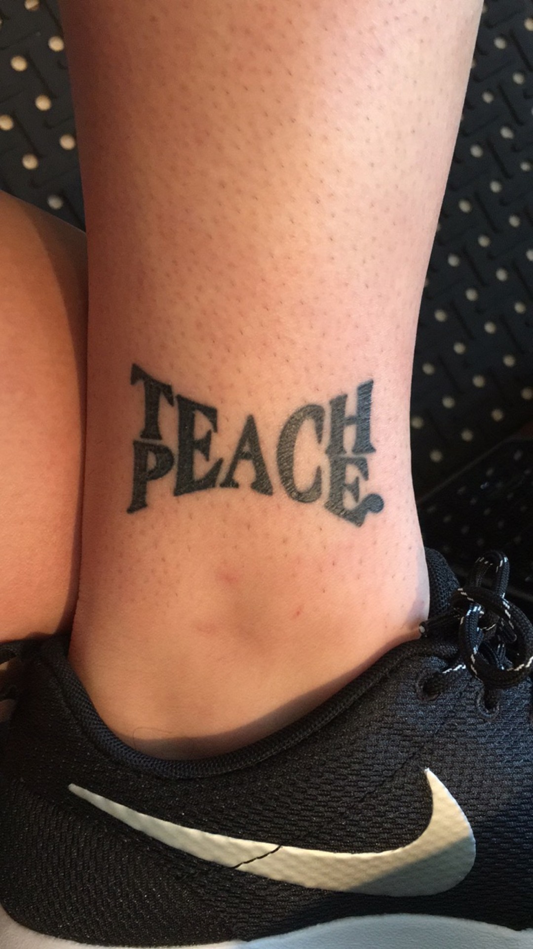 TEACH PEACE lettering tattoo on the forearm