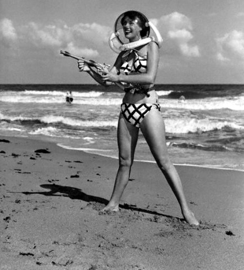 Bunny Yeager pointing a ray gun, wears a space helmet with her bikini on Miami Beach,