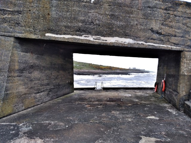 Through the gap looking towards Dunstanburgh Castle. Craster harbour, Northumberland, UK.