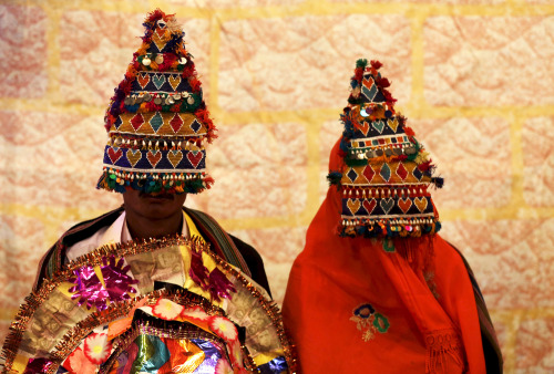 A  bride and groom wearing traditional handmade garlands wait for their wedding to start during a ma