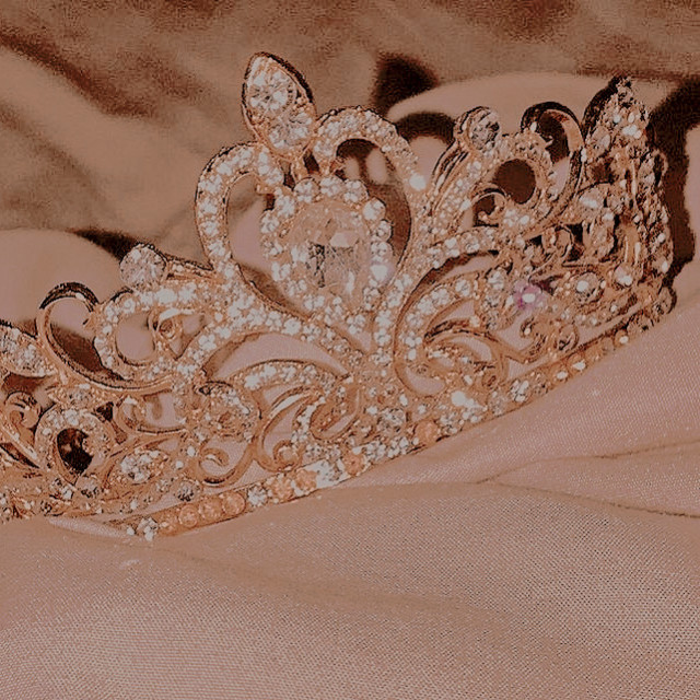 an elaborate diamond encrusted gold crown lying on rumpled pale pink sheets.