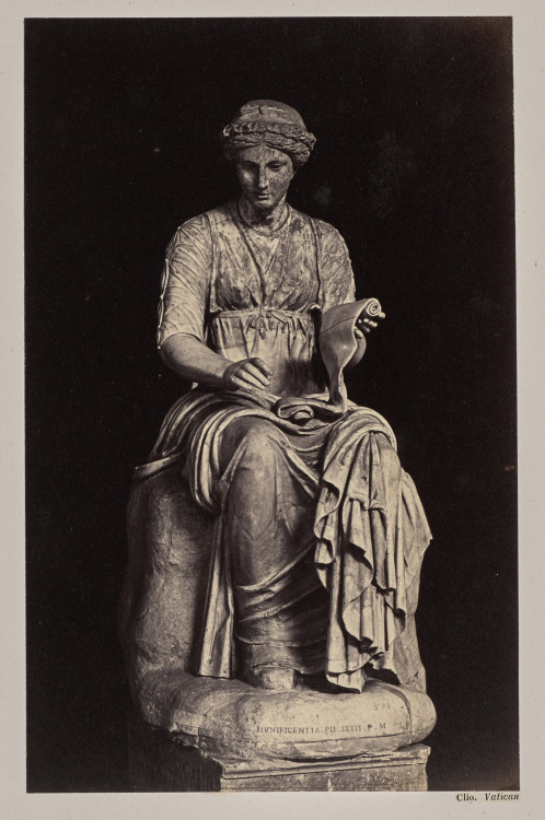 A statue of the Greek muse Clio, or Kleio. She is seated and is holding one end of a scroll, which i