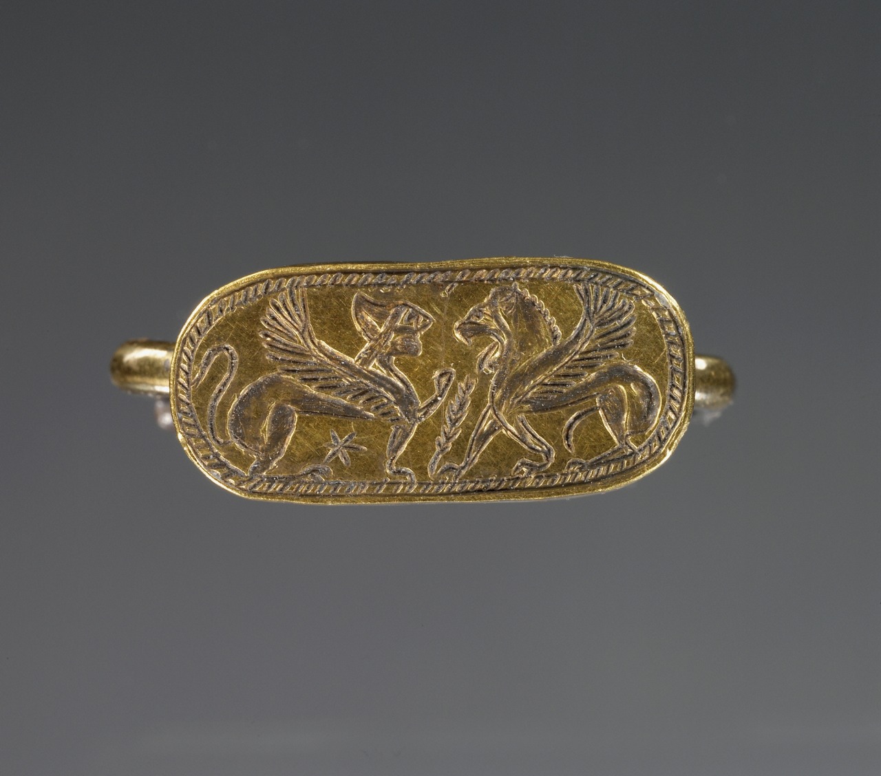 The style of this ring was introduced by immigrant Greek goldsmiths from Ionia. Its shape, long straight sides and rounded edges, is derived from Egyptian and Phoenician cartouche-shaped rings. What a beautiful meeting of cultures!
Winged Lion and...
