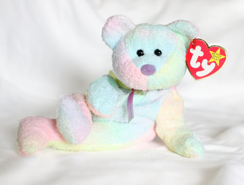 source[id: photo of a pastel rainbow tie dye bear plush, on a white cloth backdrop. it has black bea