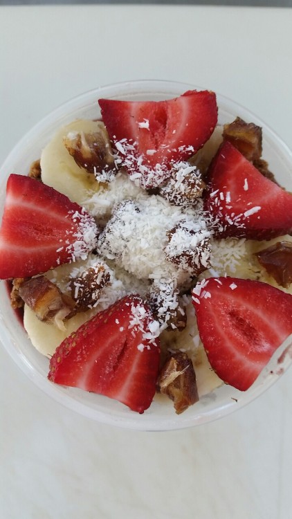Raspberry Acai bowl layered with granola, banana, strawberries, chopped dates, and coconut shavings