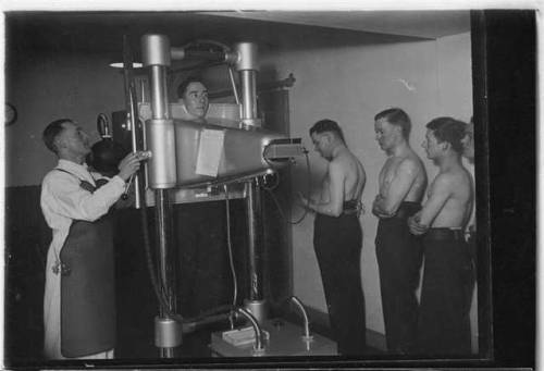 Navy recruits queuing up at base, while a radiographer positions oneof them for a chest X-ray.During