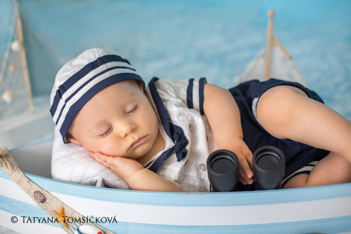 Cute toddler baby boy sleeping in wooden boat with fishes, starf