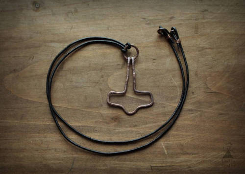 A minimalist hand-hammered Mjolnir necklace, made of copper. The pendant hangs from a 60 cm leather 