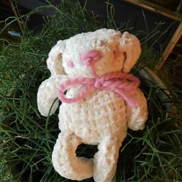 A pink and white knitted dog with closed eyes sitting on a reindeer fern
