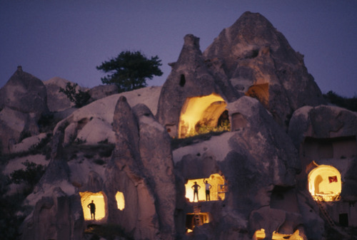 juliettegomes: unrar:Figures stand in the doorways of ancient cave dwellings, Cappadocia, Turkey, by