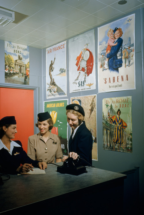 Flight attendants stand and talk beneath airline advertising posters, March 1951.Photograph by B. An